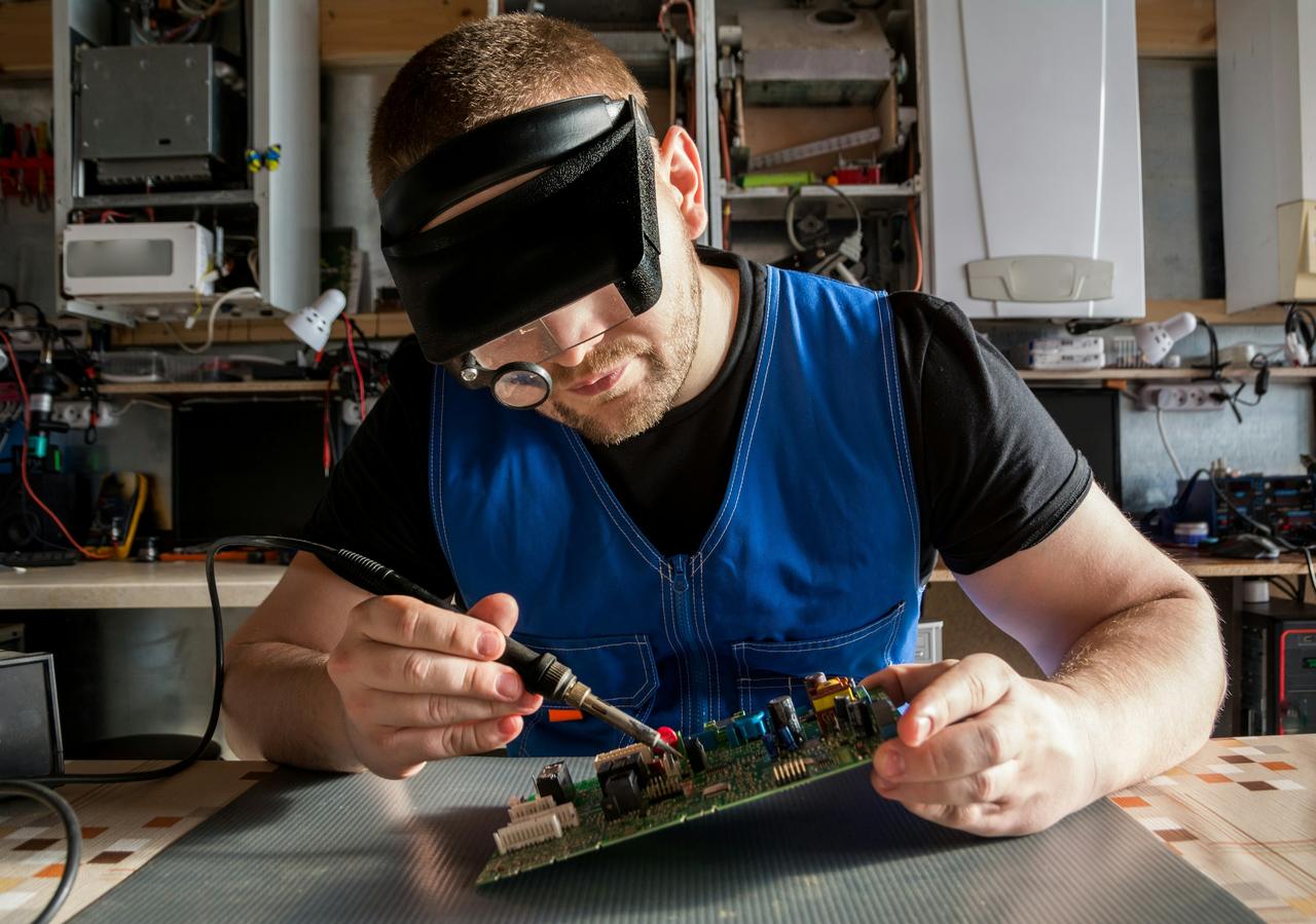 Techniker mit Lupenbrille lötet ein Bauteil auf einer Steuerplatine